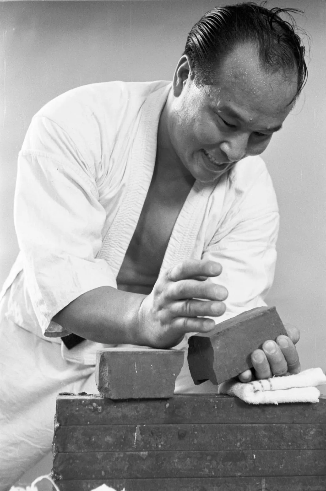 Masutatsu Oyama bricht lächelnd einen Ziegelstein mit bloßer Hand – Tameshiwari Demonstration des Kyokushin Karate Gründers