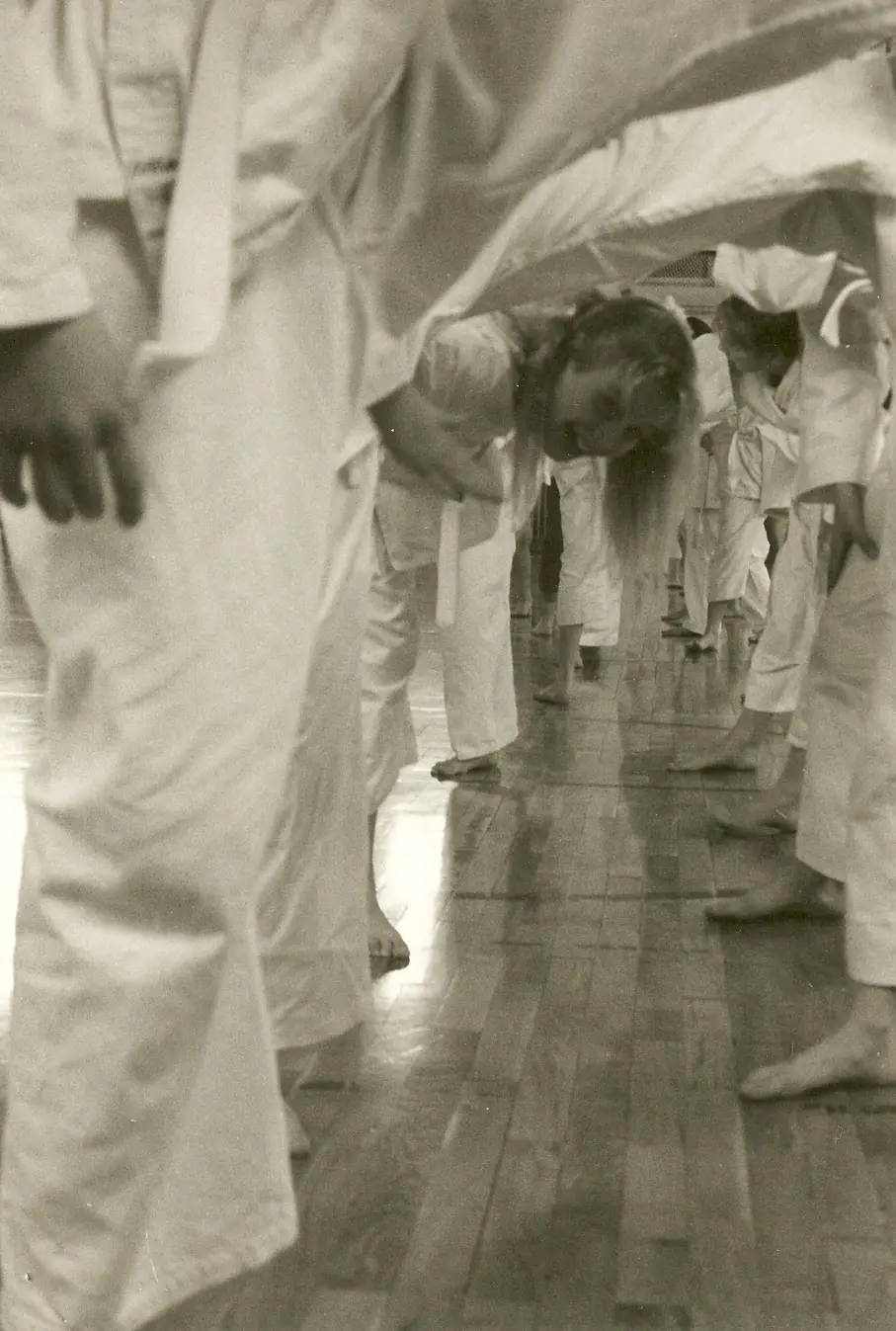 Spaß beim Beine-hoch-Training Karateka des Kyokushinkai Karate Köpenick e.V. heben im Vordergrund die Beine hoch, während eine Frau lustig darunter hindurchschaut, im ehemaligen Dojo im Alexander-von-Humboldt-Gymnasium