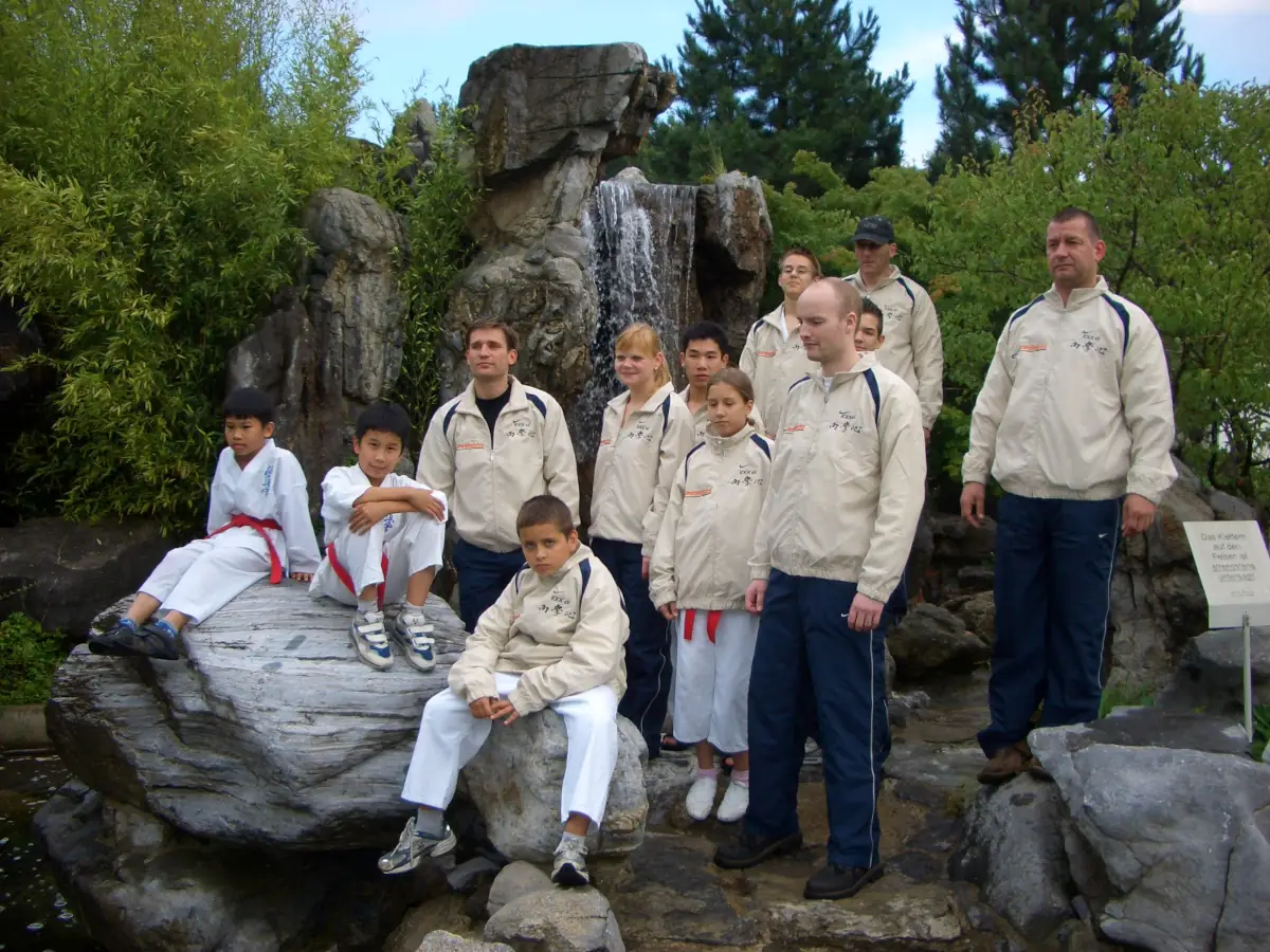 KKK e.V. – Gärten der Welt mit Sponsorenanzügen der Ossege GmbH (2007) Karateka des Kyokushinkai Karate Köpenick e.V. vor einem Wasserfall in den Gärten der Welt Berlin im Jahr 2007.