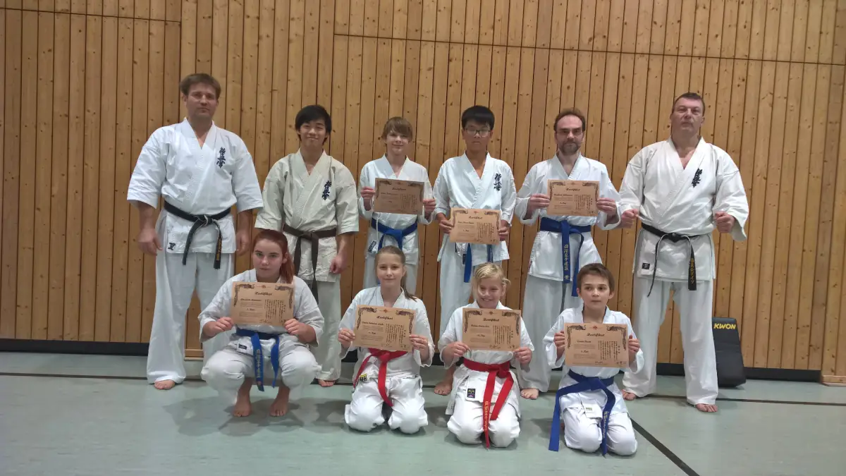 KKK e.V. Gürtelprüfung (Kyu) 2015 Eine Gruppe von Karateka im weißen Gi steht und kniet mit ihren Prüfungsurkunden in einer Sporthalle bei der Gürtelprüfung des KKK e.V.